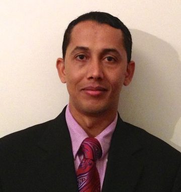 Dr. Shyam Sharma in a suit with mauve shirt and tie