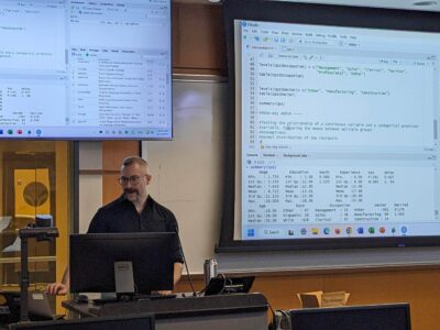 A staff member presents in front of a screen of code at a statistical workshop