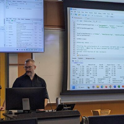 A staff member presents in front of a screen of code at a statistical workshop