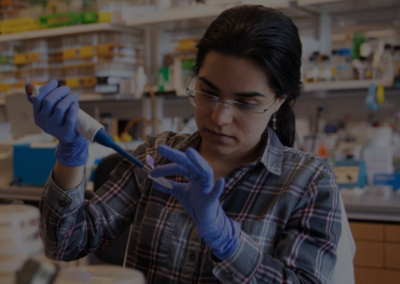 Gloved woman in glasses and a plaid shirt using a pipette in a laboratory