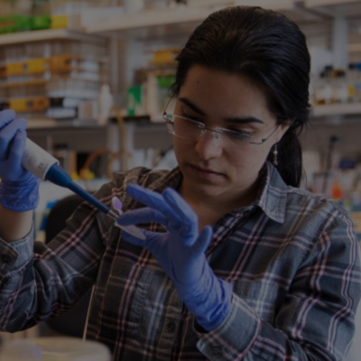 Gloved woman in glasses and a plaid shirt using a pipette in a laboratory