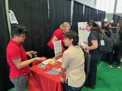 Staff in red shirts talking to students at a booth in a resource fair.