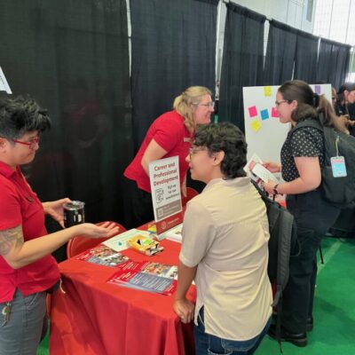 Staff in red shirts talking to students at a booth in a resource fair.