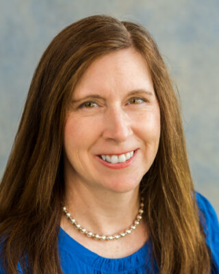 Smiling woman in a necklace and blue shirt.