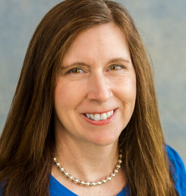Smiling woman in a necklace and blue shirt.